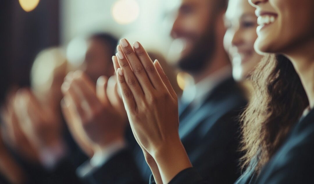 Un grupo de personas aplaudiendo en un entorno profesional, captando un gesto de reconocimiento y motivación en el trabajo. La imagen refleja el compromiso y celebración en el ámbito laboral, relacionado con los servicios de formación de Kapacita.